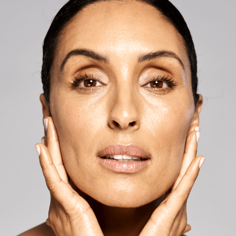 Close-up of a woman holding her face with a neutral expression, clear complexion, subtle makeup.