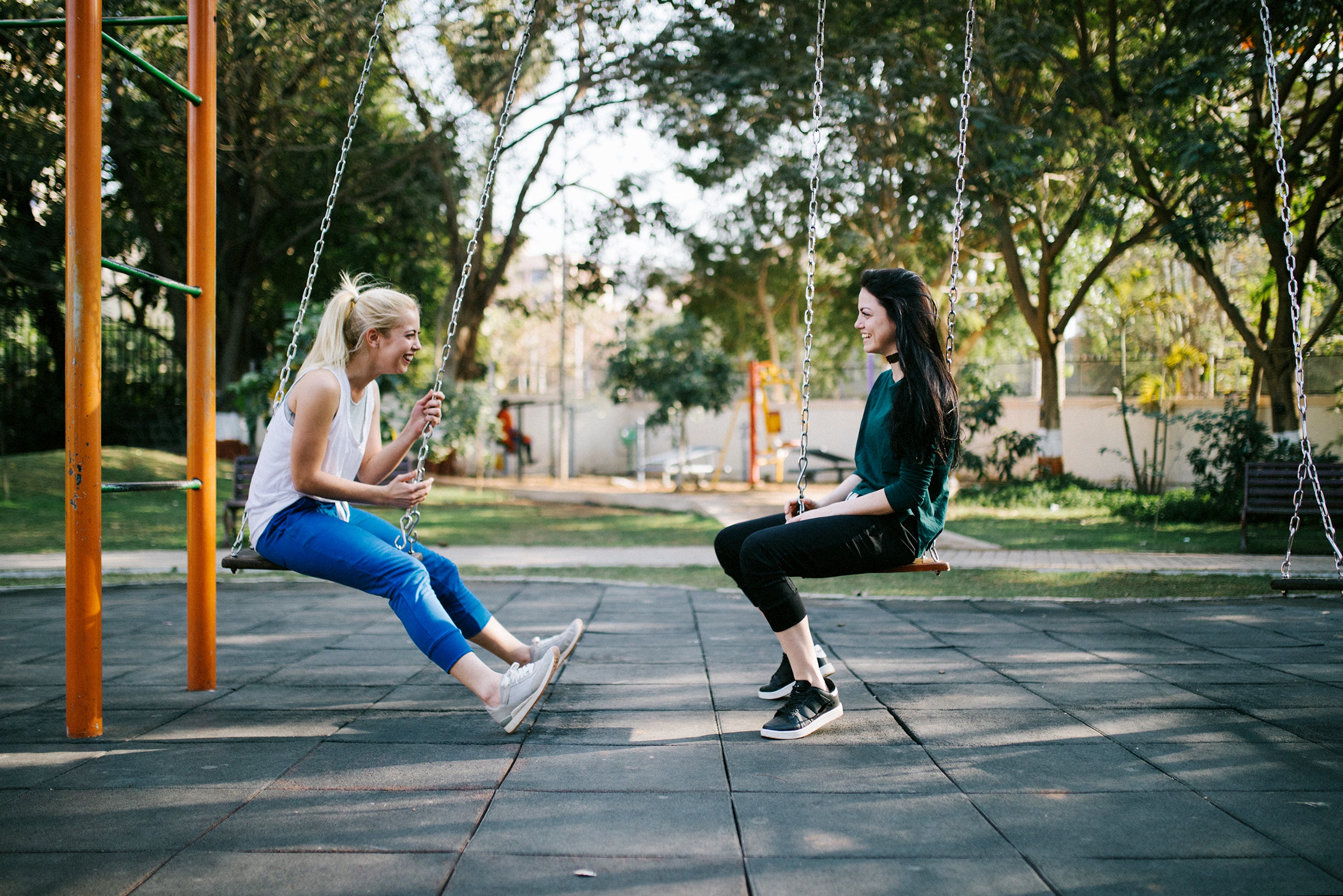 two women sitting across from each other on swings