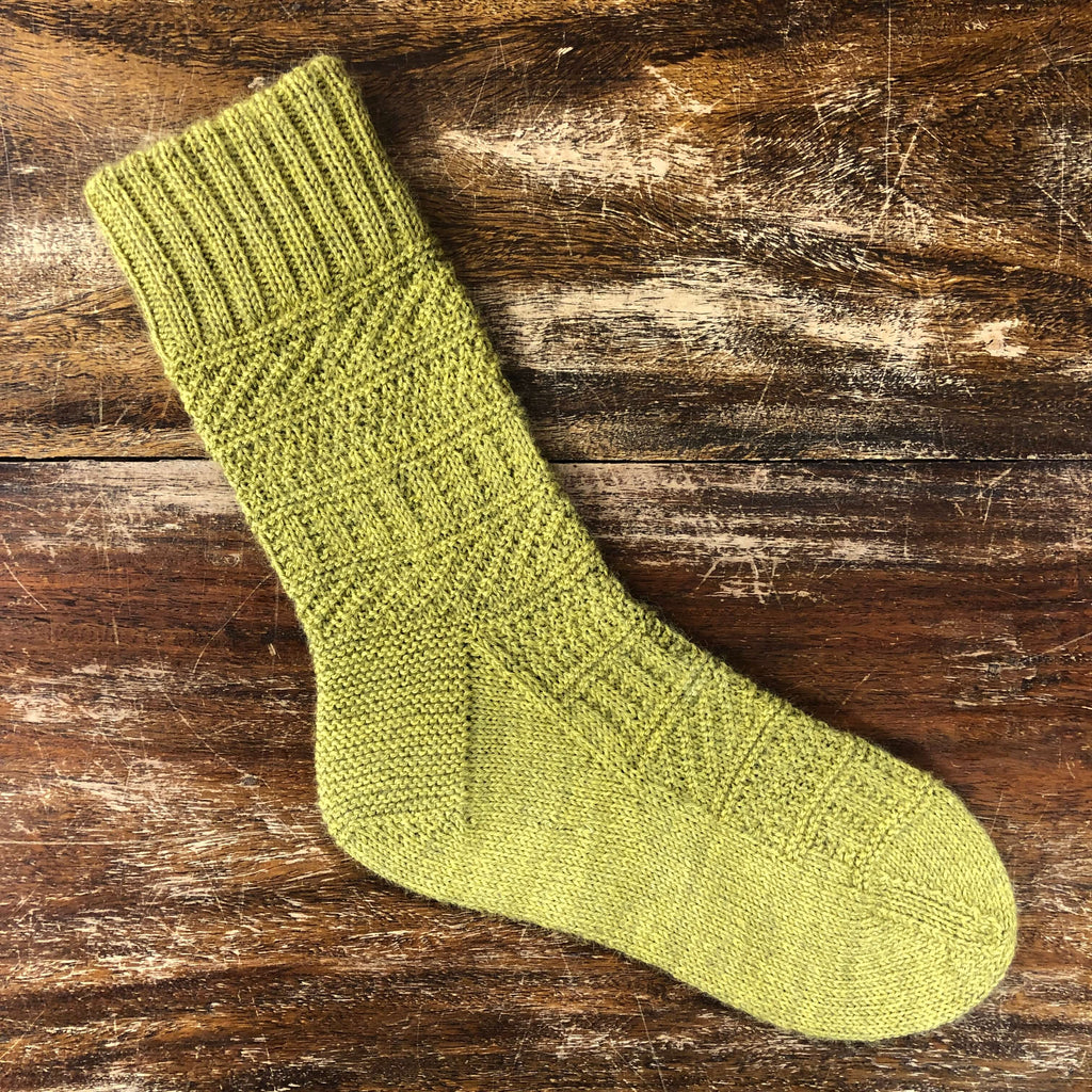 greeny yellow hand knitted sock on a wooden table