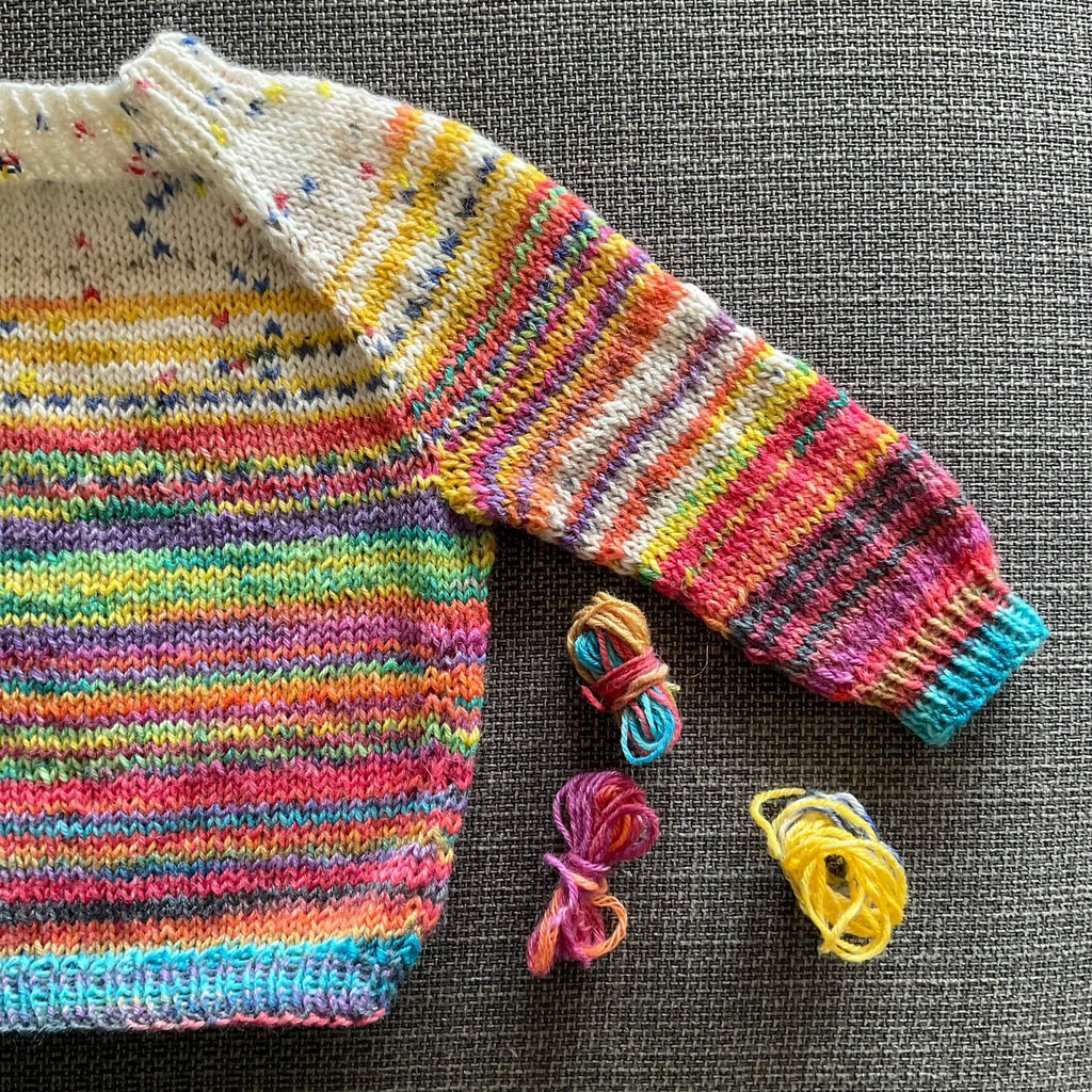 multicoloured baby jumper with small balls of yarn