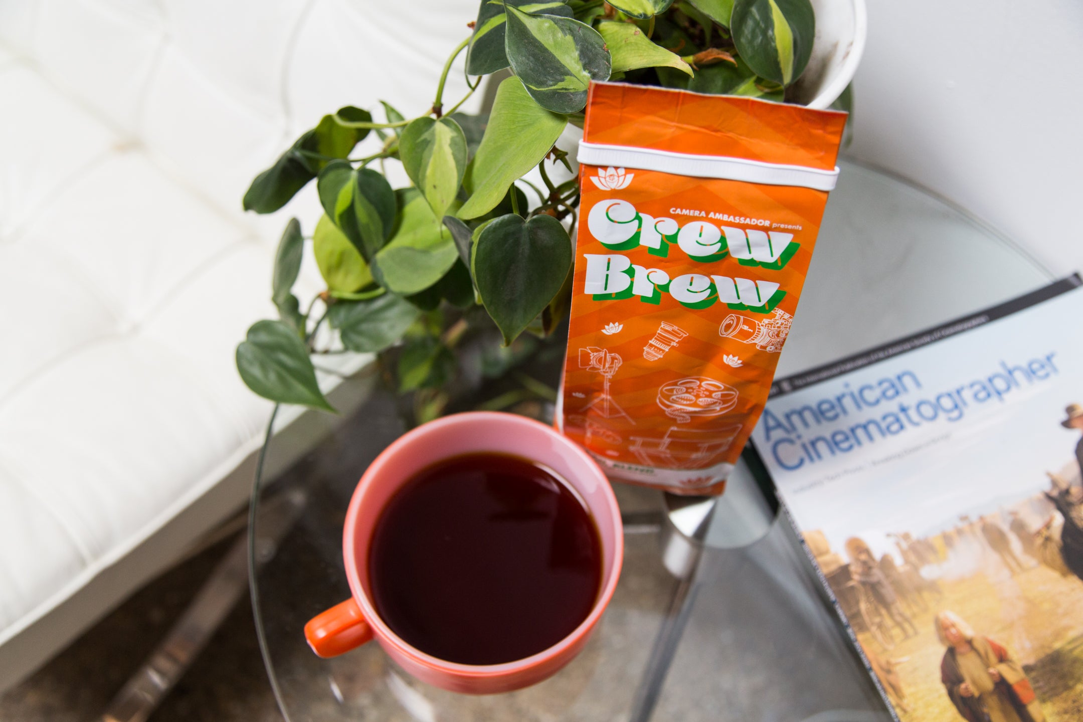 lifestyle photo of crew brew on a coffee table, next to a plant and a magazine "American Cinematographers"