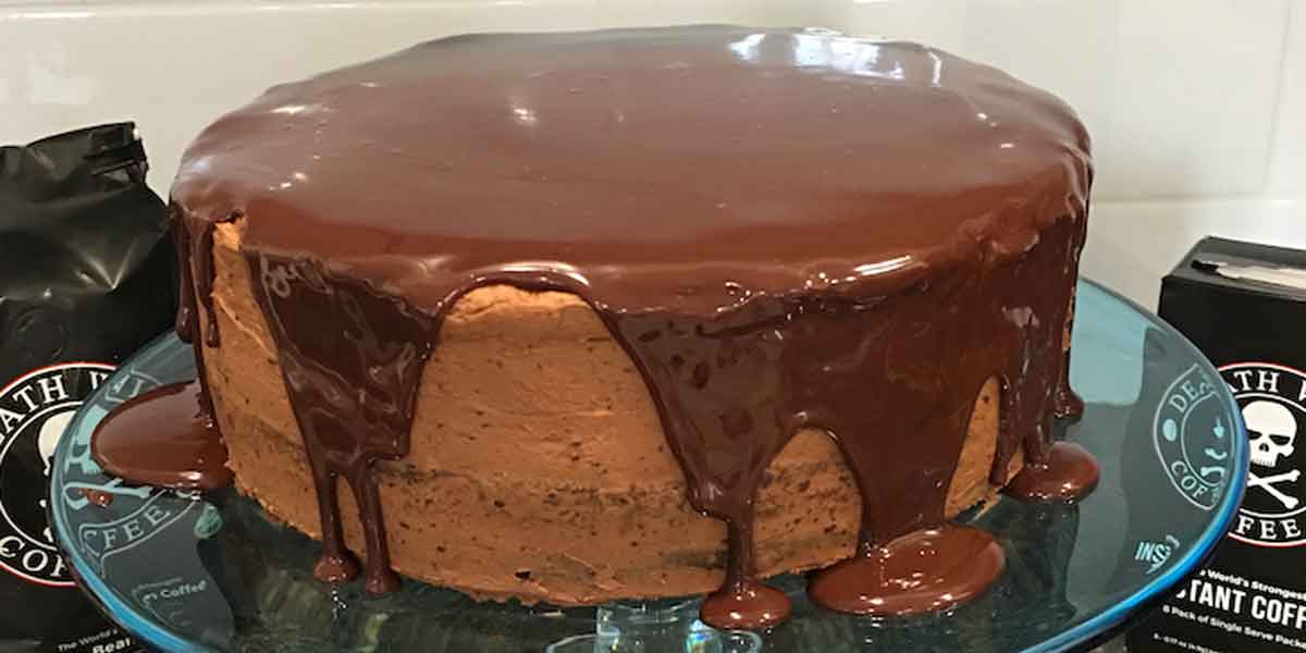 A chocolate cake on a cake stand with a chocolate ganache