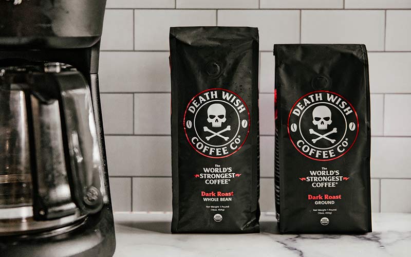 A white kitchen counter with a coffee maker and two red + black bags of Death Wish OG Dark Roast Coffee.