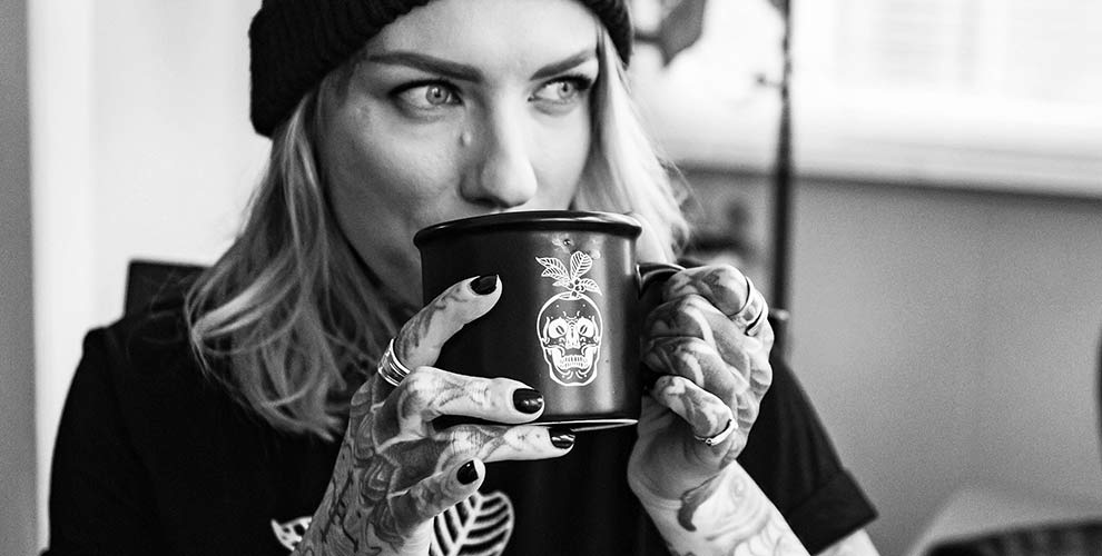 A female with blonde hair sipping out of a black coffee mug.