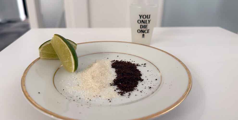 Limes, coffee and sugar on a white plate next to a shot of tequila