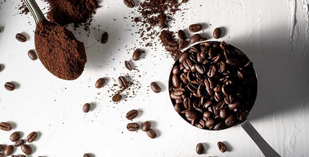 spoon with ground coffee and measuring cup with whole bean coffee