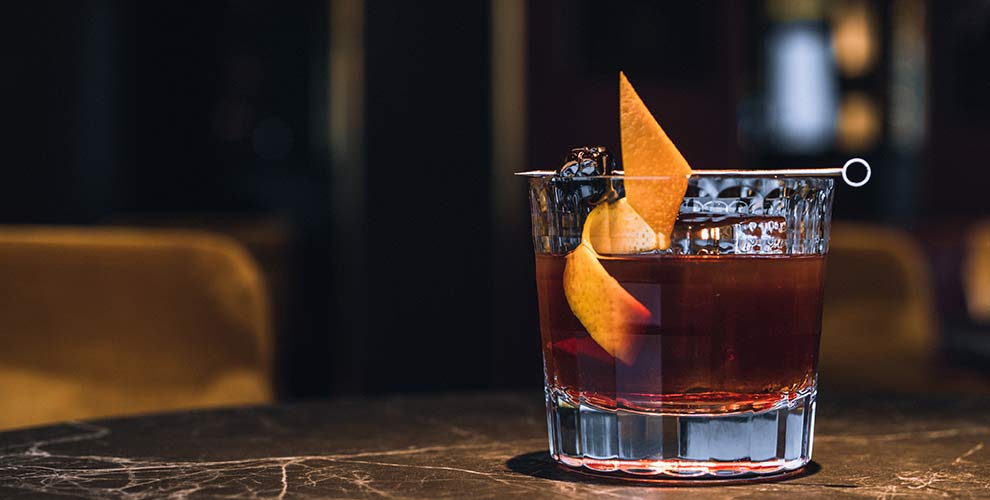 A coffee based old fashioned cocktail with a lemon peel as a garnish.