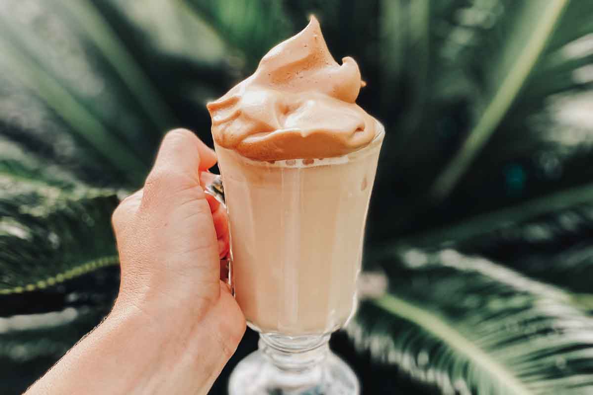 A hand holding a glass of whipped coffee