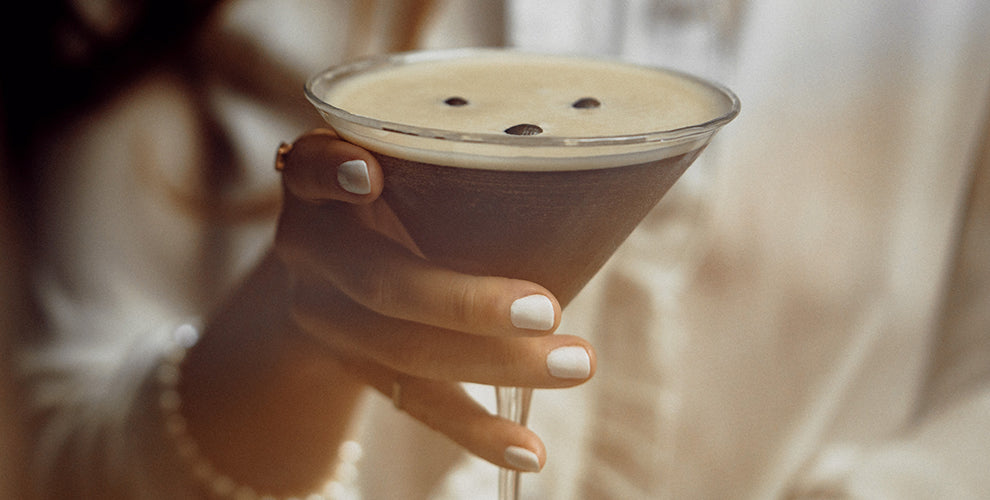 A woman with white nail polish holding a cold brew martini.
