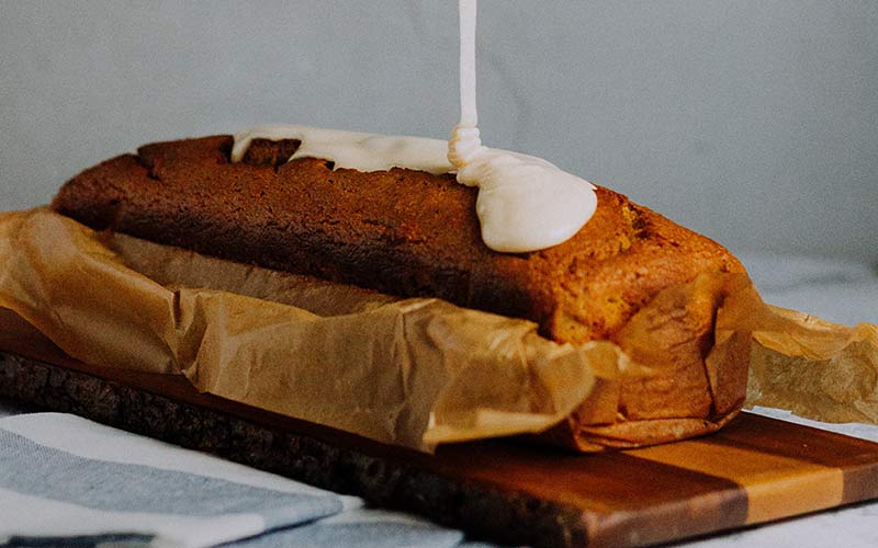 A loaf of gingerbread on top of a wooden cutting board with frosting dribbling on top.