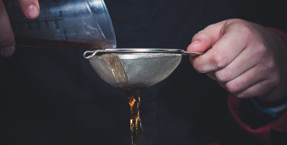 A man holding a small strainer to separate the grounds out of the coffee using the strainer method.