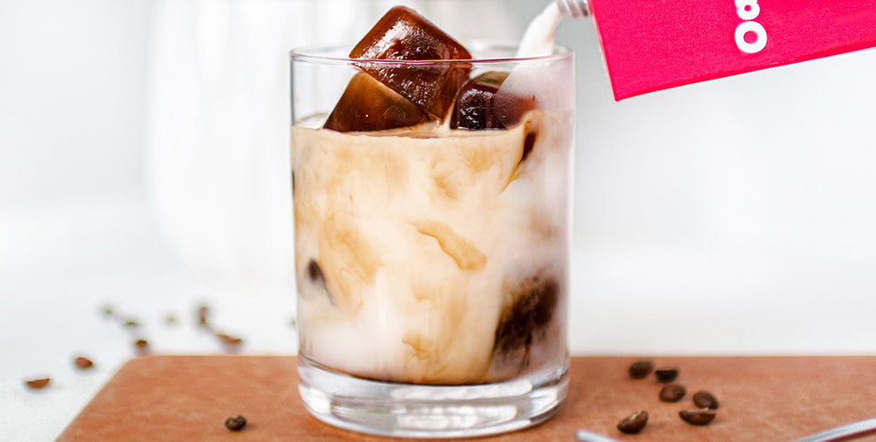 A glass of iced coffee with coffee ice cubes and milk being poured into the glass.