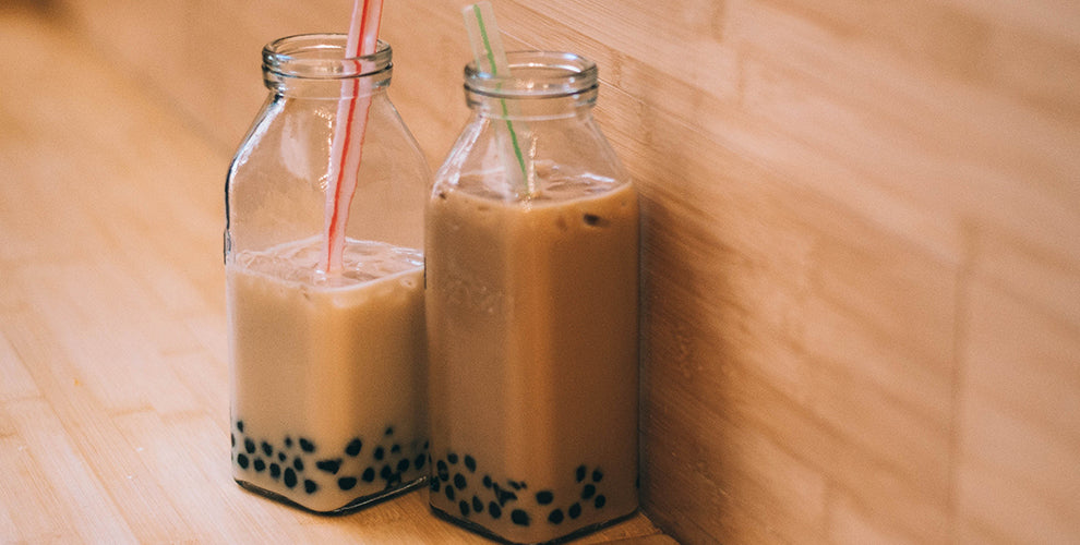 Two glass bottles of iced boba coffee with plastic straws.