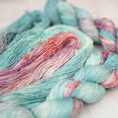 Three skeins of variegated yarn in half pale aqua and half speckled (with blue, purple and orange speckles). 