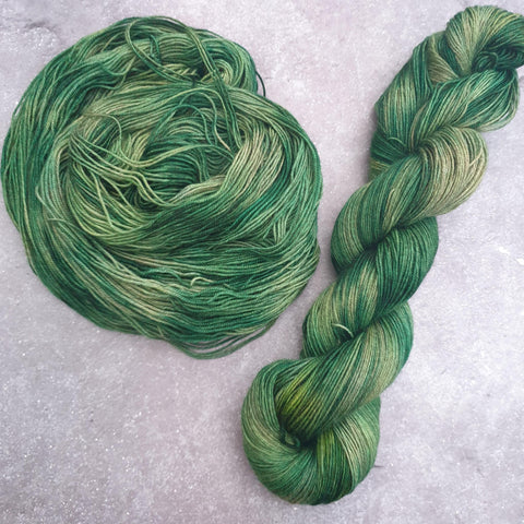 Two green tonal skeins of yarn on a yak blend, one twisted and one spiraling around itself to form a circle.