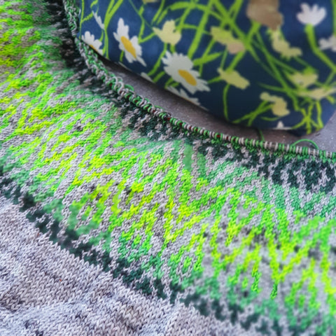 An unfinished colourwork sweater with a grey main colour and a dark, forest green fading in to a neon green for contrast.