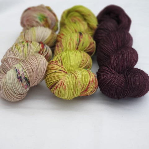 three skeins of yarn, one light with speckles, one mustard with speckles and one a dark burgundy.