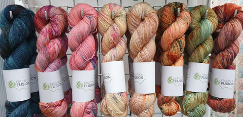 A line of eight vivid but autumnal coloured skeins of yarn, hanging on grid wall hooks