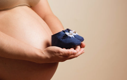a belly of a pregnant woman holding a pair of baby shoes