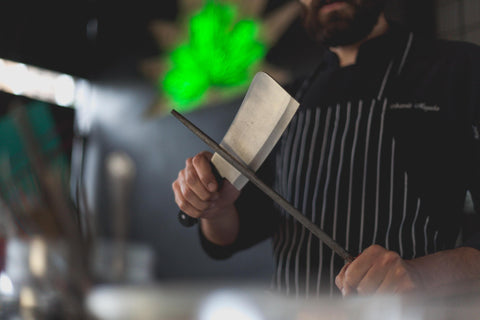 Man in Black and White Striped Apron Holding Cleaver Knife and Honing Rod