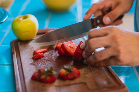 person cutting strawberries using a utility knife on a wooden board