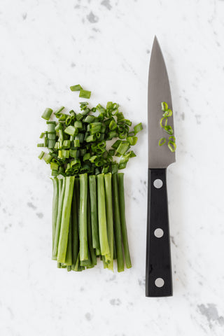 chopped green onions and paring knife on a white table