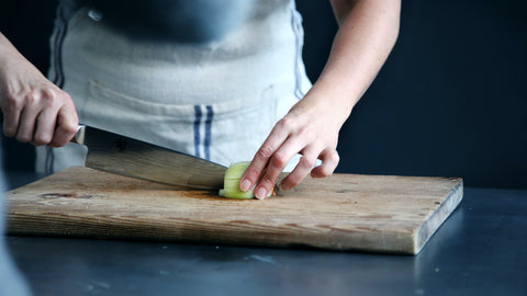 person chopping onion using chef knife on a wooden cutting board