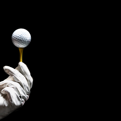 photo of a gloved hand holding a golf ball on a black background