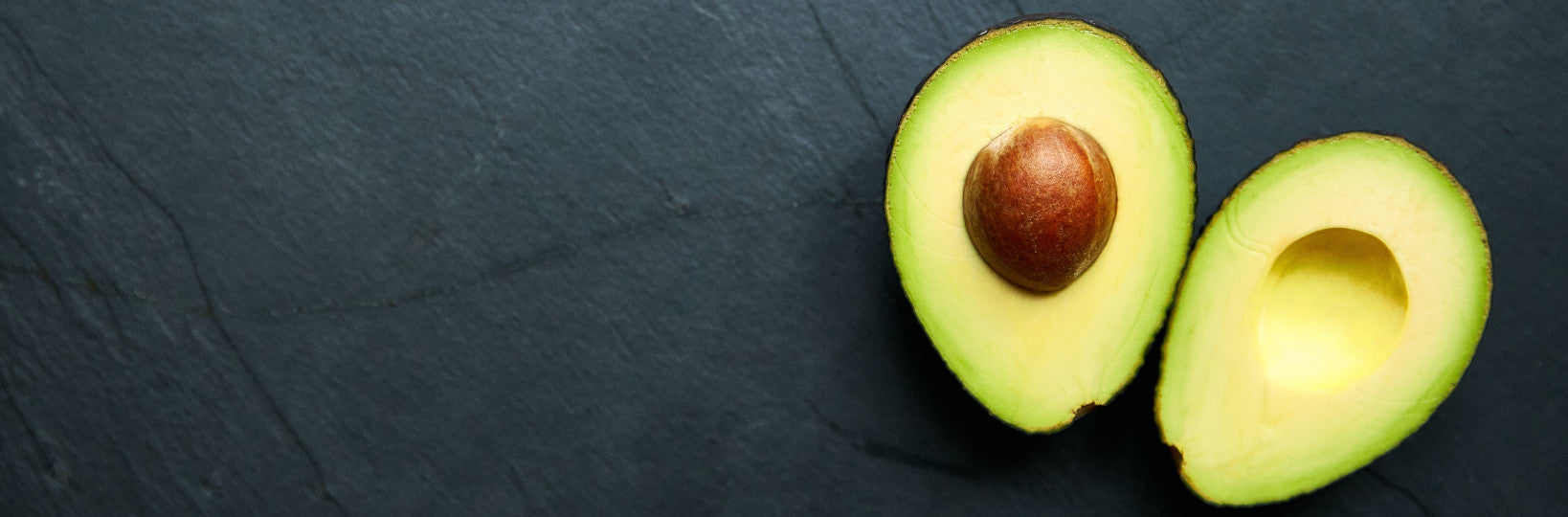 Two avocado halves on black slate 