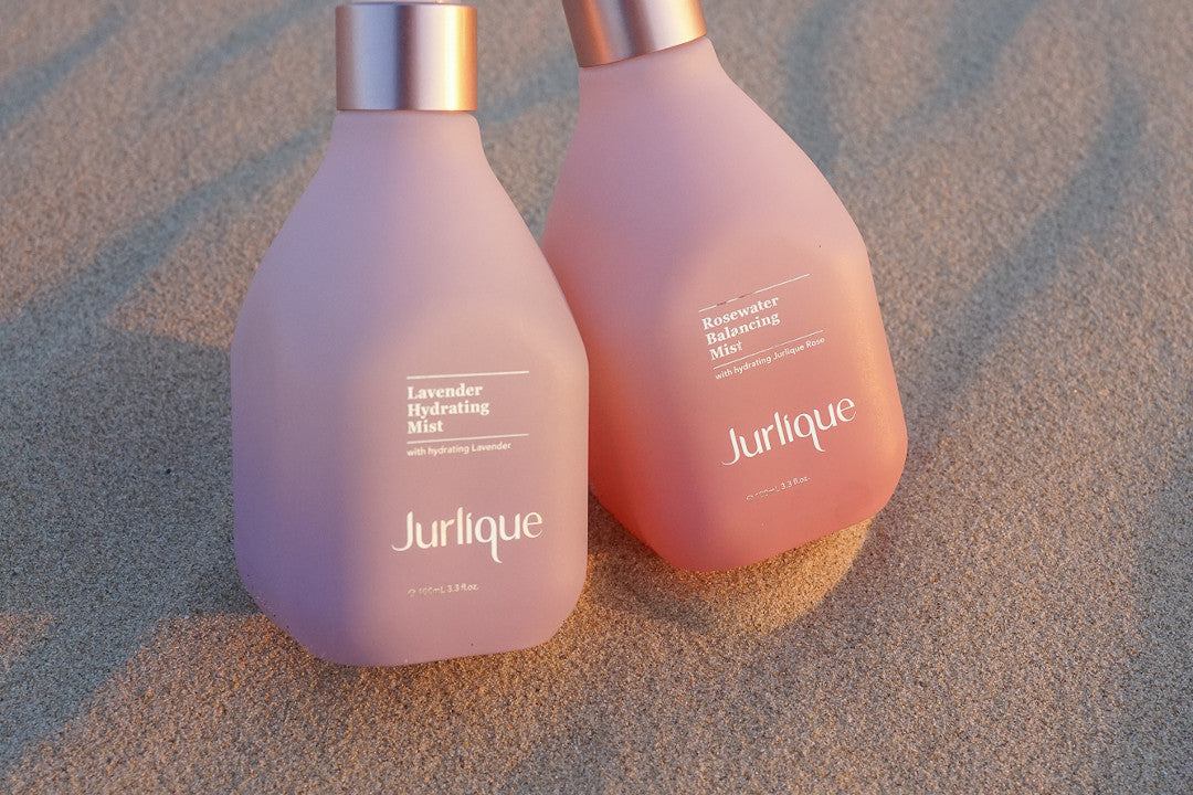 Bottles of Jurlique Lavender Hydrating Mist and Rosewater Balancing Mist next to each other on sand