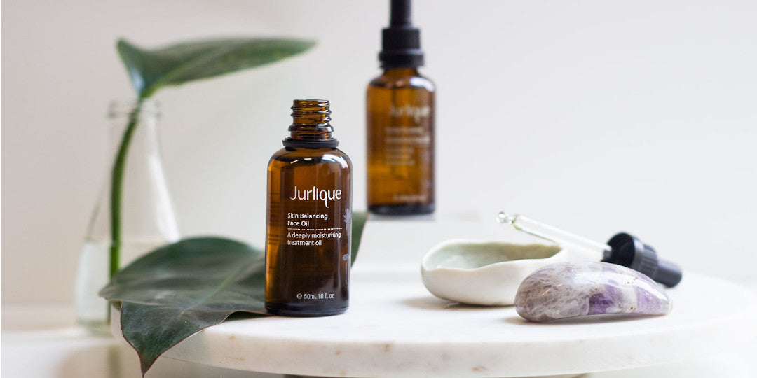 Bottle of Jurlique Skin Balancing Face Oil next to Amethyst stone and two green leaves 