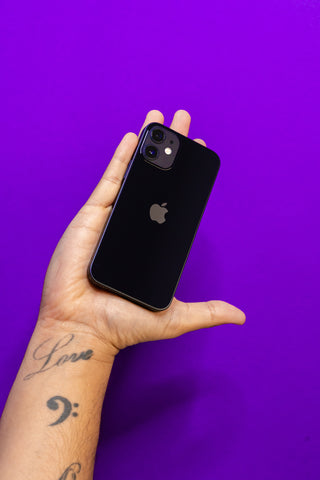 Left hand holding a black iPhone 12 against a reboxed purple background