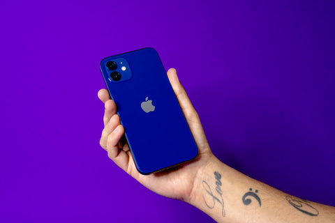 Right hand holding a blue iPhone 12 against a reboxed purple background