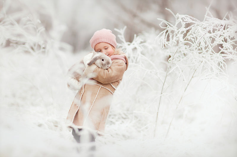 Little girl holding cold rabbit in snow.