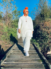 Outfit shot of person wearing white poncho and trousers with orange headscarf walking toward camera