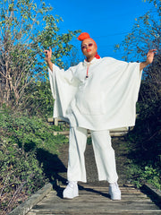 Outfit shot of person wearing white poncho and trousers with orange headscarf facing the camera