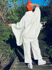 Outfit shot of person wearing white poncho and trousers with orange headscarf