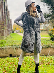 Outfit shot of person wearing grey fur waistcoat and glasses facing right