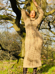 Outfit shot of person wearing beige knitted dress facing camera with arms above head posing