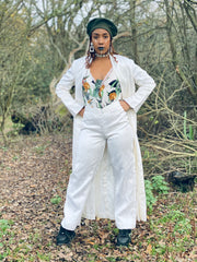 Outfit shot of woman wearing white trousers and white jacket with a green patterned top underneath facing forward with hands on hips posing