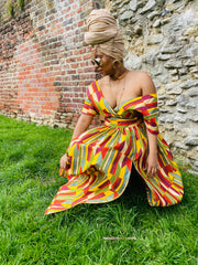 Outfit shot of person crouching wearing multi-colour gown and headscarf and sunglasses