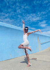 Outfit shot of person wearing white dress posing with arms in the air facing the camera