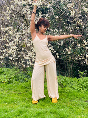 Outfit shot of person wearing beige strappy top and wide leg trousers facing the side with right arm above head and other out to the side posing