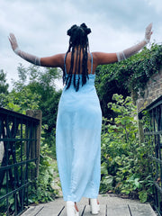 Outfit shot of person wearing long blue dress facing away from camera with arms in the air posing