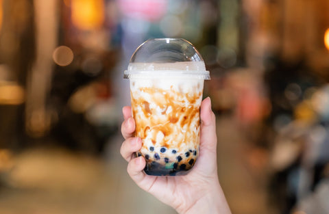 young woman is holding drinking brown sugar flavored boba tapioca pearl bubble milk tea with glass straw night market taiwan close up bokeh