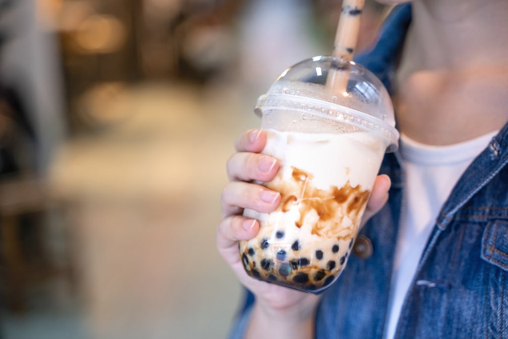 young woman is holding drinking brown sugar flavored tapioca pearl bubble milk tea boba with glass straw night market taiwan close up bokeh