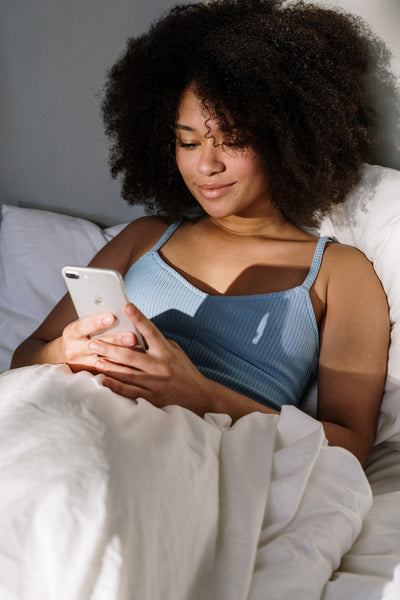 woman with curly hair in bed reading phone