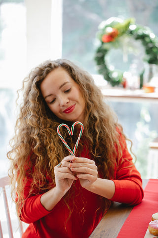 woman with curly hair holding candy canes in the shape of a heart