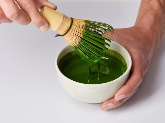 Thick liquid matcha tea in bowl with matcha whisk, held by hand