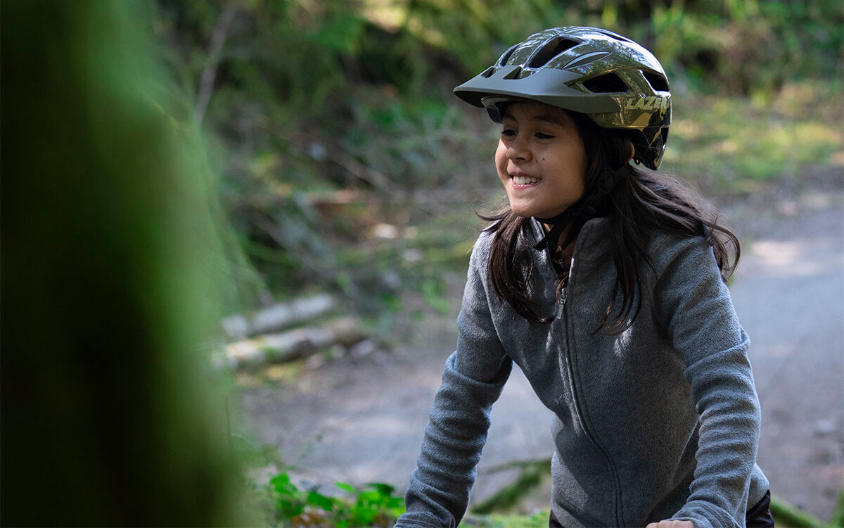 Girl riding her mountain bike wearing a green Lazer Gekko MIPS kids bike helmet